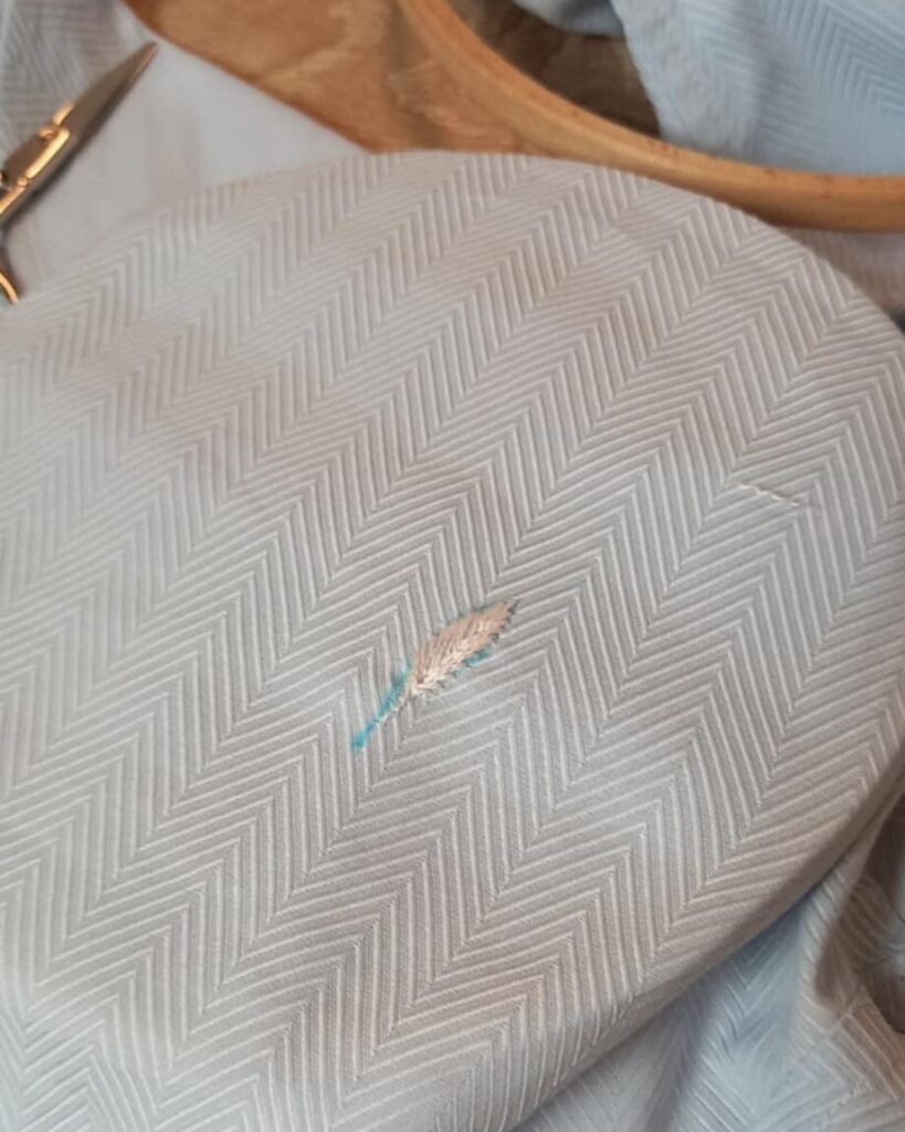 Réparation textile d'une chemise par la broderie : broderie en cours. La plume est brodée sur le marqueur.
