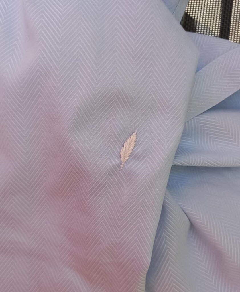 Réparation textile d'une chemise par la broderie : Résultat final sans marqueur, après rinçage. Broderie de plume blanche sur chemise en coton bleue et blanche.